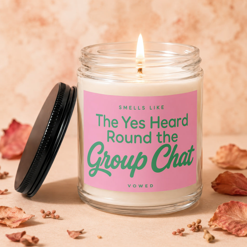 Lit candle in glass jar with pink label reading "Smells like The Yes Heard Round the Group Chat".