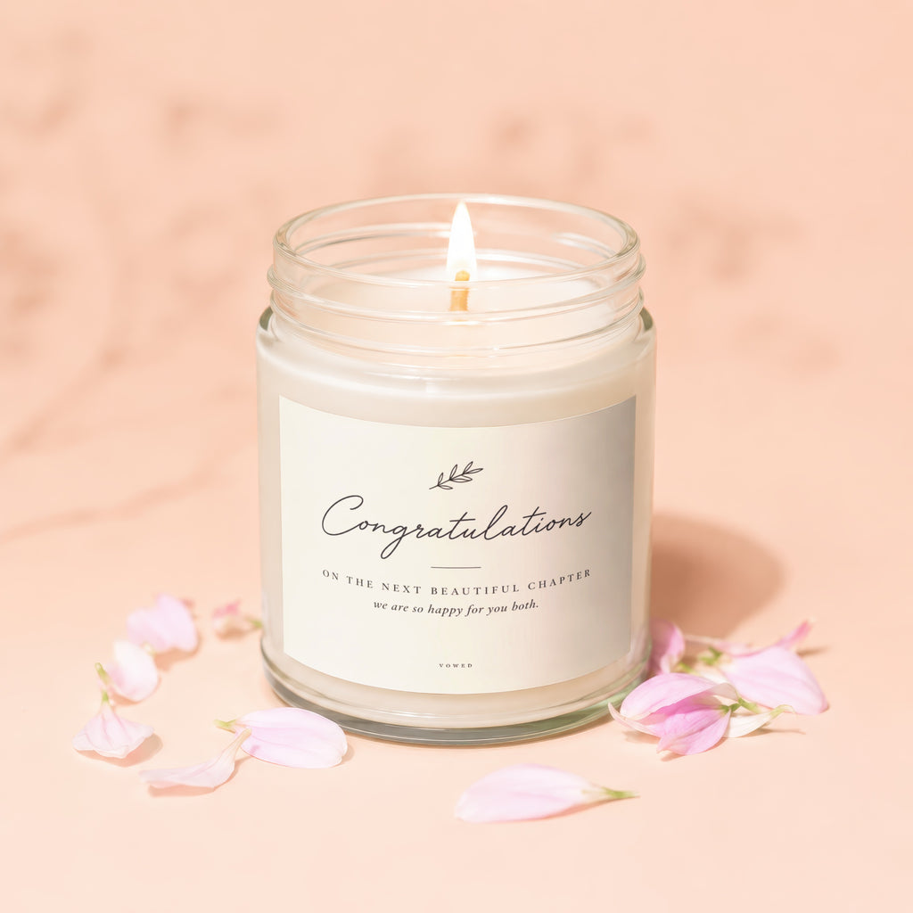 Candle with "Congratulations" label, pink petals on peach background.