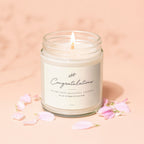 Candle with "Congratulations" label, pink petals on peach background.