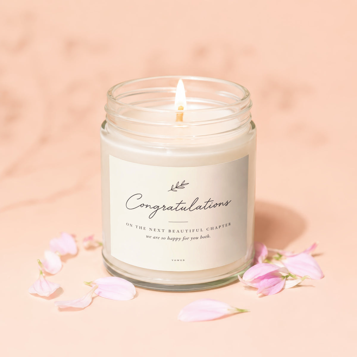 Candle with "Congratulations" label, pink petals on peach background.
