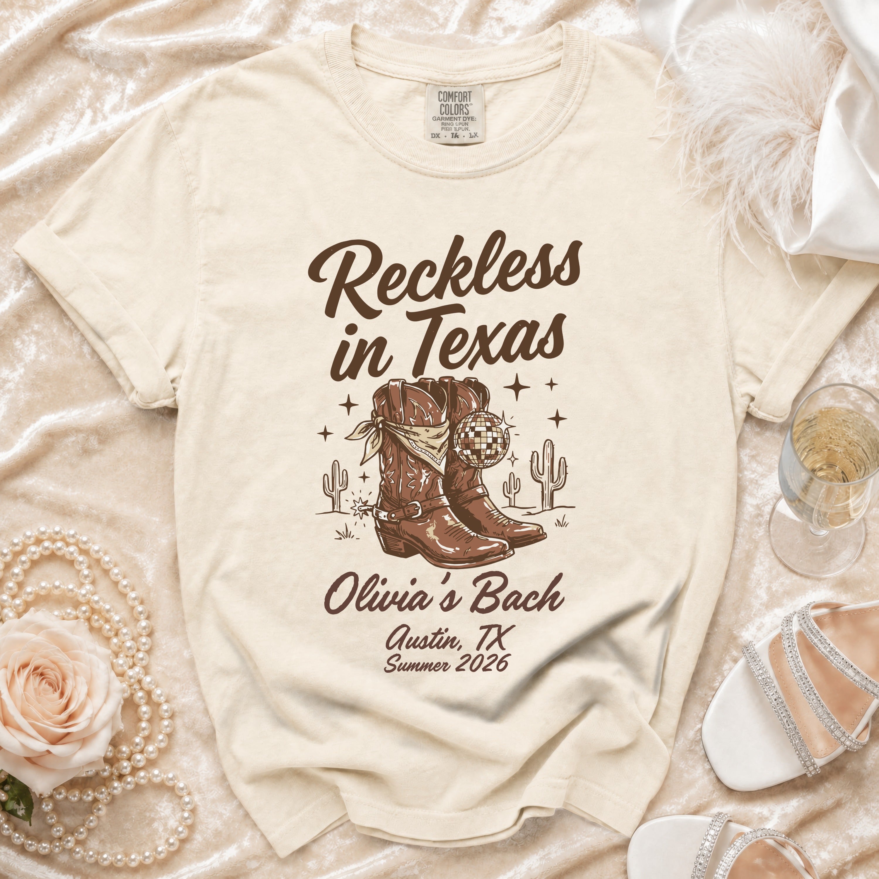 Cream t-shirt with "Reckless in Texas" and cowboy boots graphic, "Olivia's Bach Austin, TX Summer 2026".