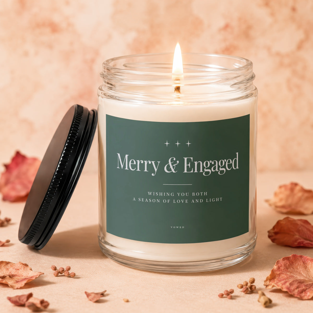 Glass candle with "Merry & Engaged" label, lit wick, and black lid.