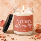 Lit candle in glass jar with "Partners, officially VOWED" text on label.