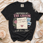 Black t-shirt with "Mother of the Groom" text and floral envelope design.