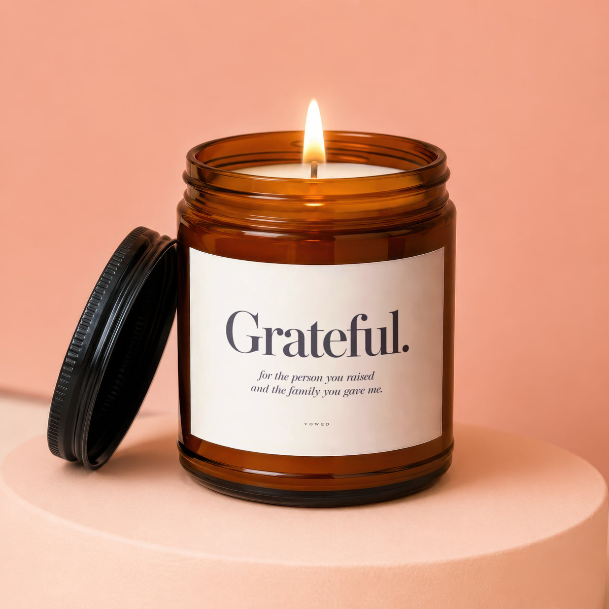 Amber glass candle with lit wick and lid. Label reads "Grateful."
