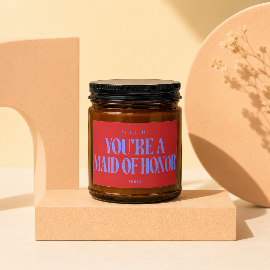 Brown candle with red label that says "Smells Like You're a Maid of Honor".