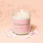 Clear glass candle with a peach label reading "bridesmaid noun" and descriptive text.