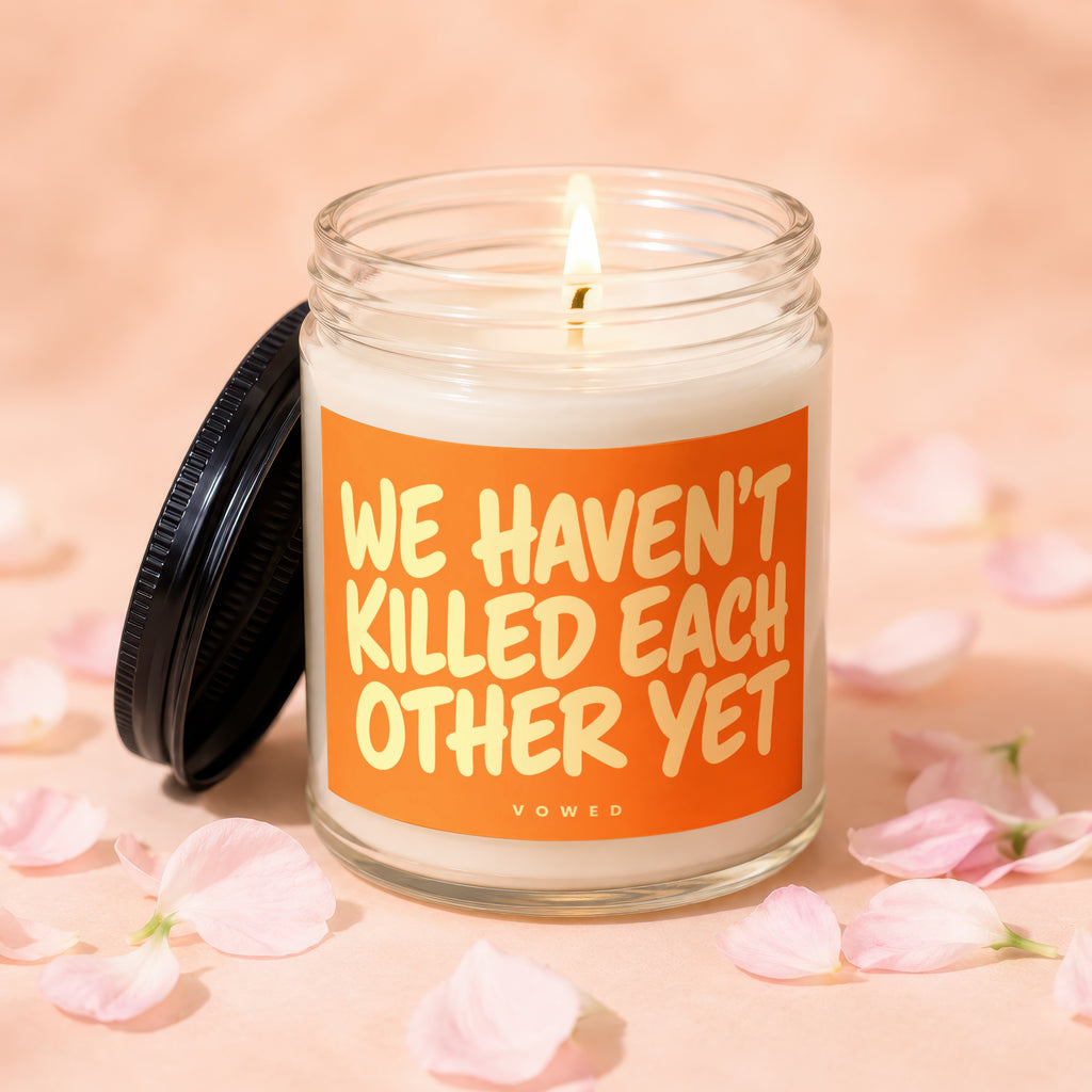 Lit candle in a jar with orange label reading "WE HAVEN'T KILLED EACH OTHER YET"