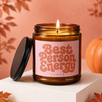 Amber jar candle with lit flame, pink label reads "Best Person Energy VOWED".