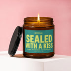 Brown glass candle with lit wick and teal label reading "OFFICIAL: SEALED WITH A KISS".
