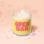Candle with "OPEN BAR LOADING..." text on a bright yellow label, surrounded by pink petals.