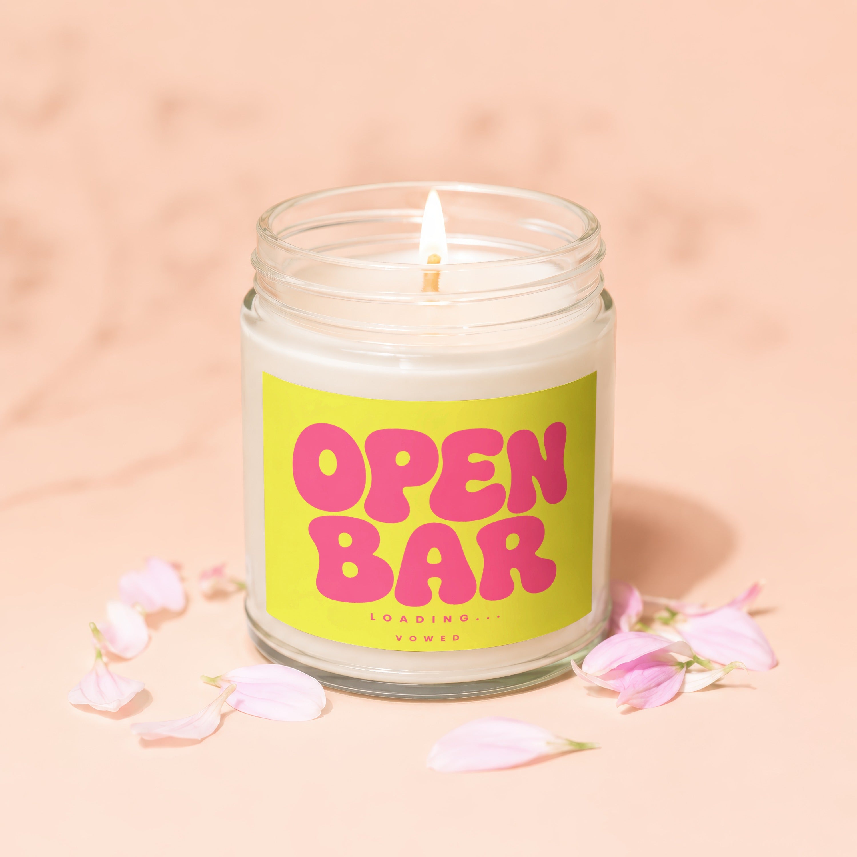 Candle with "OPEN BAR LOADING..." text on a bright yellow label, surrounded by pink petals.