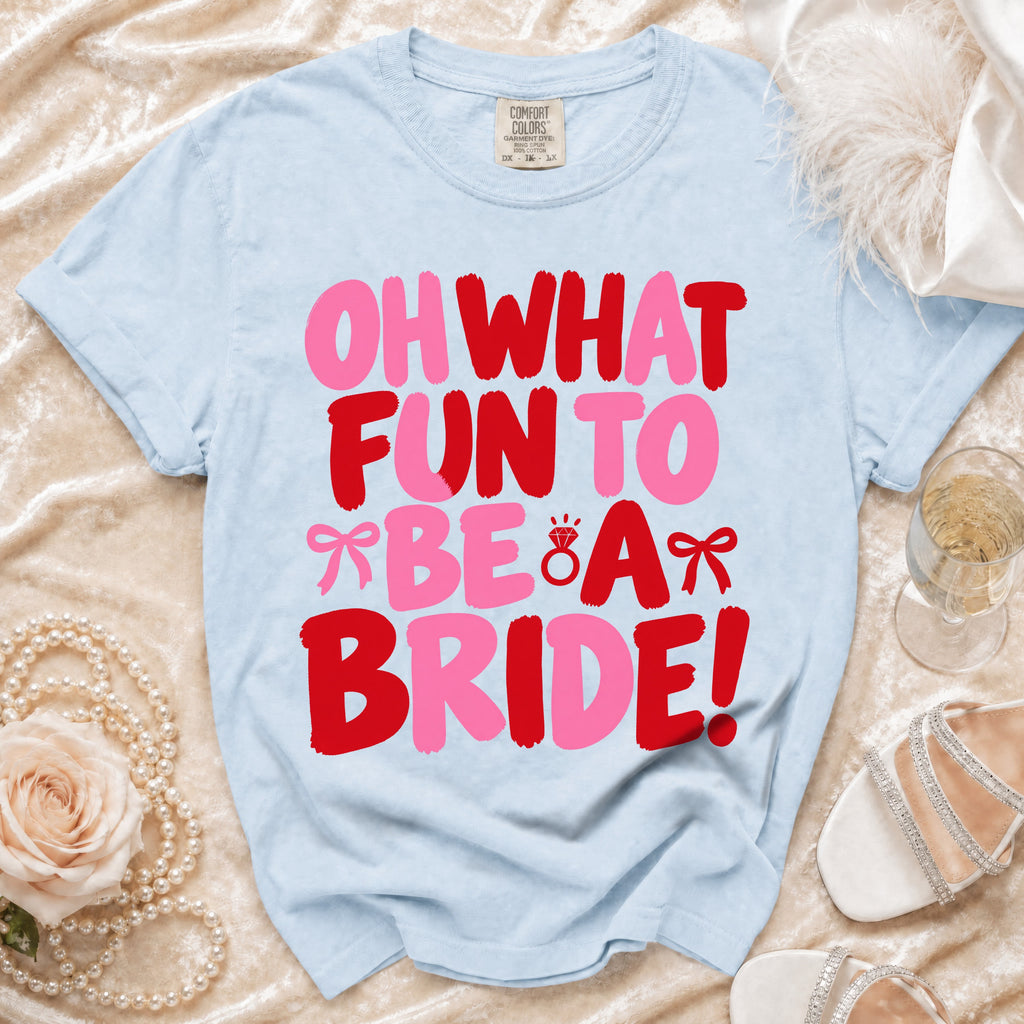Light blue t-shirt featuring pink and red text reading Oh What Fun To Be A Bride surrounded by wedding accessories.