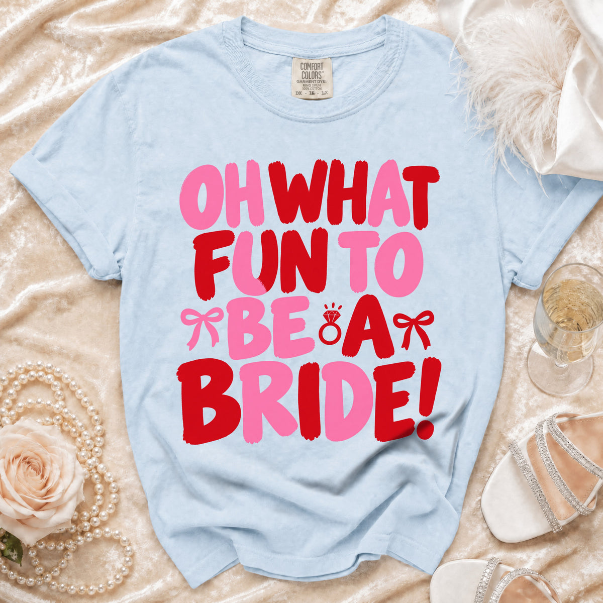 Light blue t-shirt featuring pink and red text reading Oh What Fun To Be A Bride surrounded by wedding accessories.