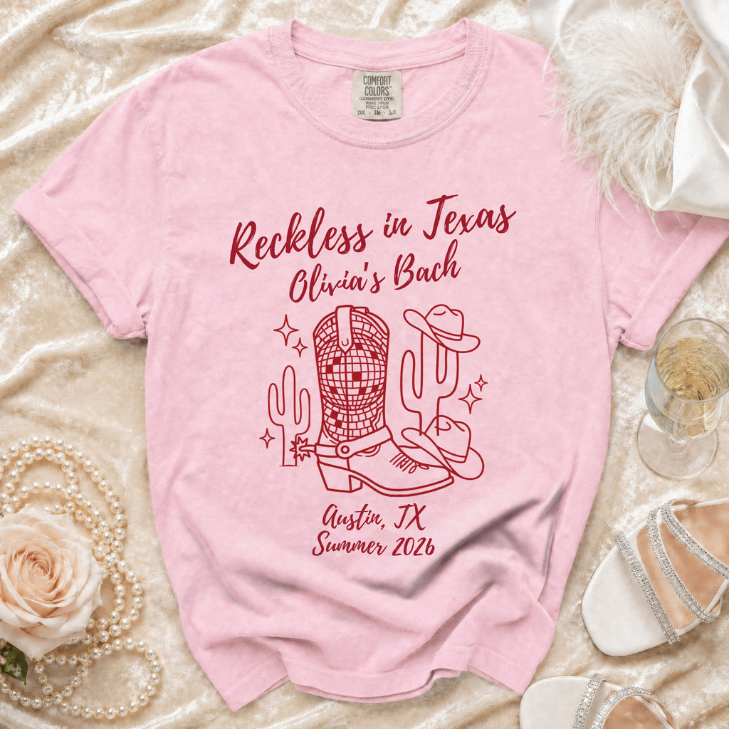 Pink t-shirt with "Reckless in Texas Olivia's Bach Austin, TX Summer 2026" and cowboy motifs.