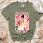 Green t-shirt with "BRIDE TO BE" graphic featuring a bride, flowers, ring, and champagne glasses.