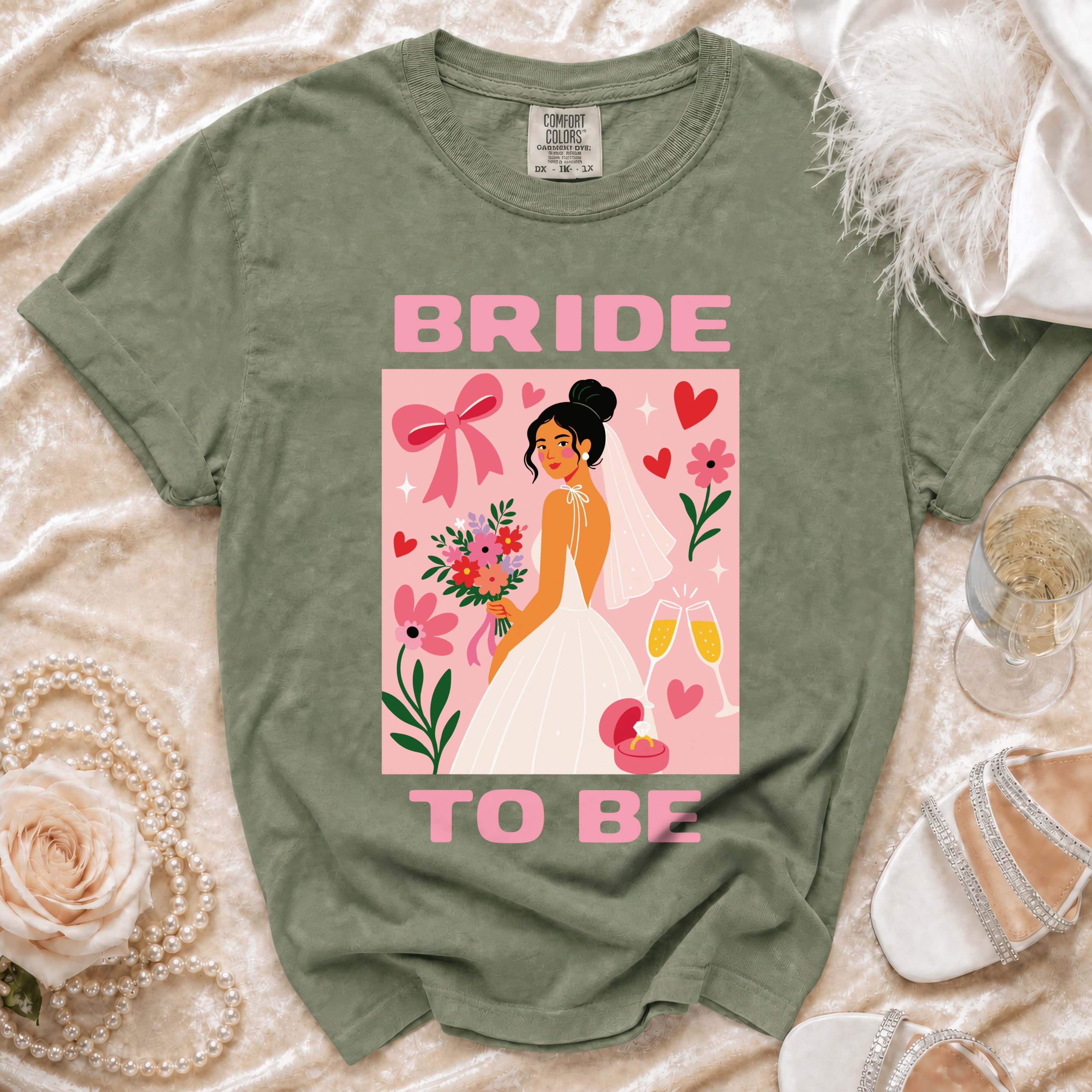 Green t-shirt with "BRIDE TO BE" graphic featuring a bride, flowers, ring, and champagne glasses.