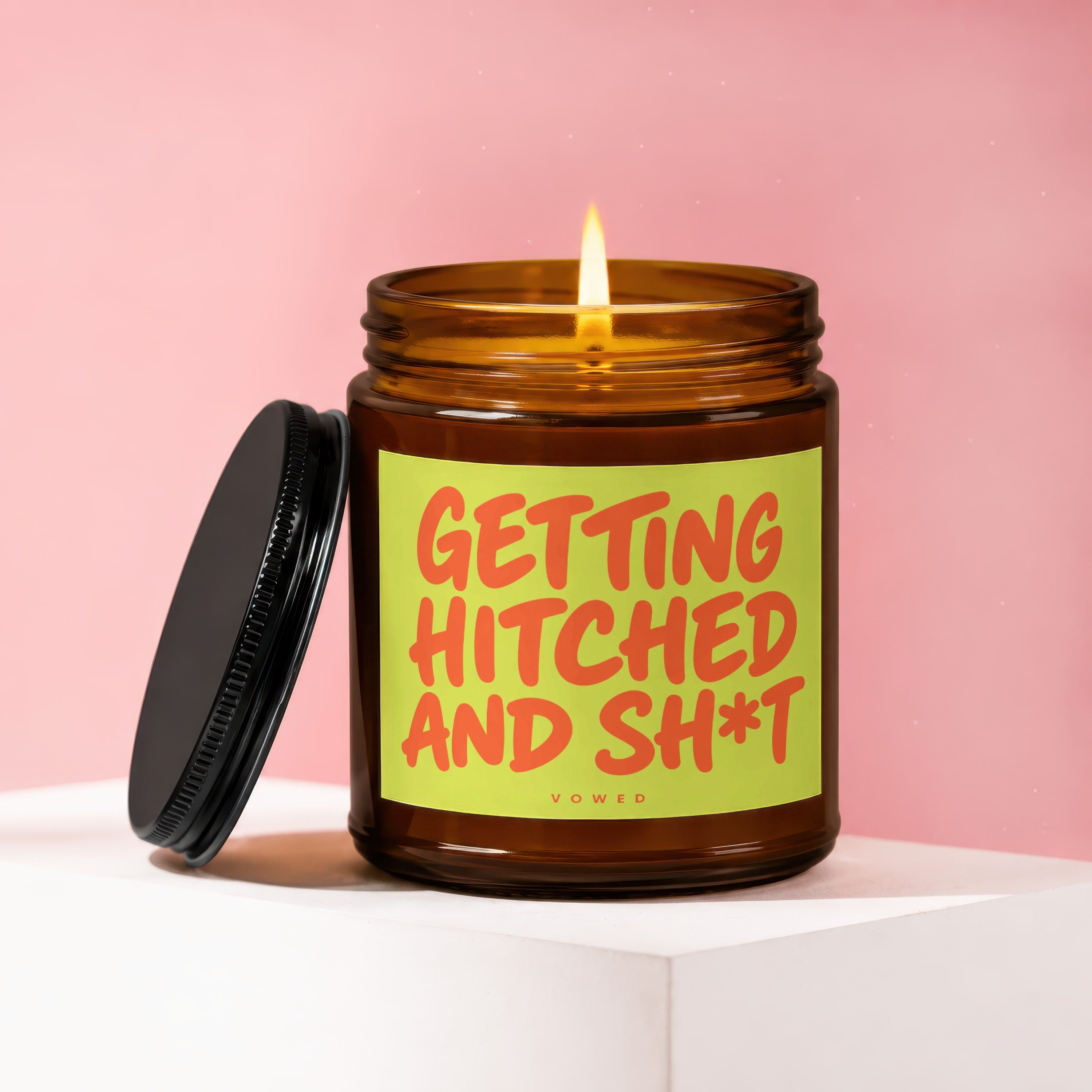Amber candle with lit flame and black lid, reads "GETTING HITCHED AND SH*T".