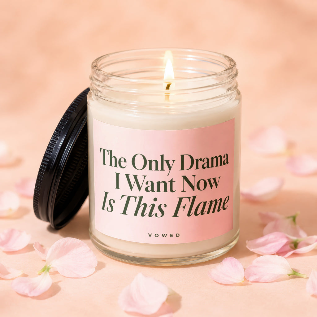 Glass candle with lit flame, black lid, and pink label; "The Only Drama I Want Now Is This Flame"