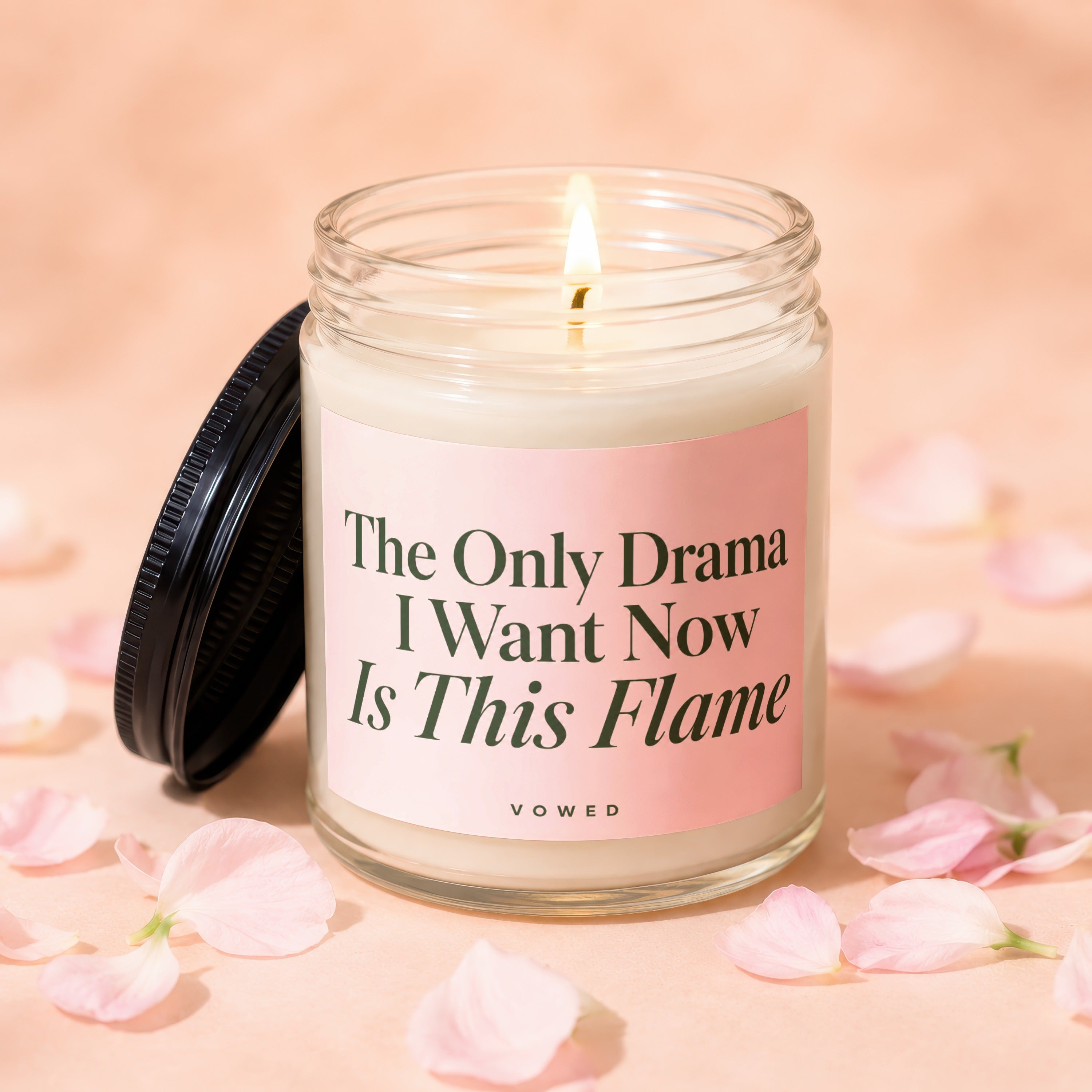 Glass candle with lit flame, black lid, and pink label; "The Only Drama I Want Now Is This Flame"