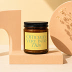 Brown glass candle with yellow label reading "Officially Very Into This vowed".