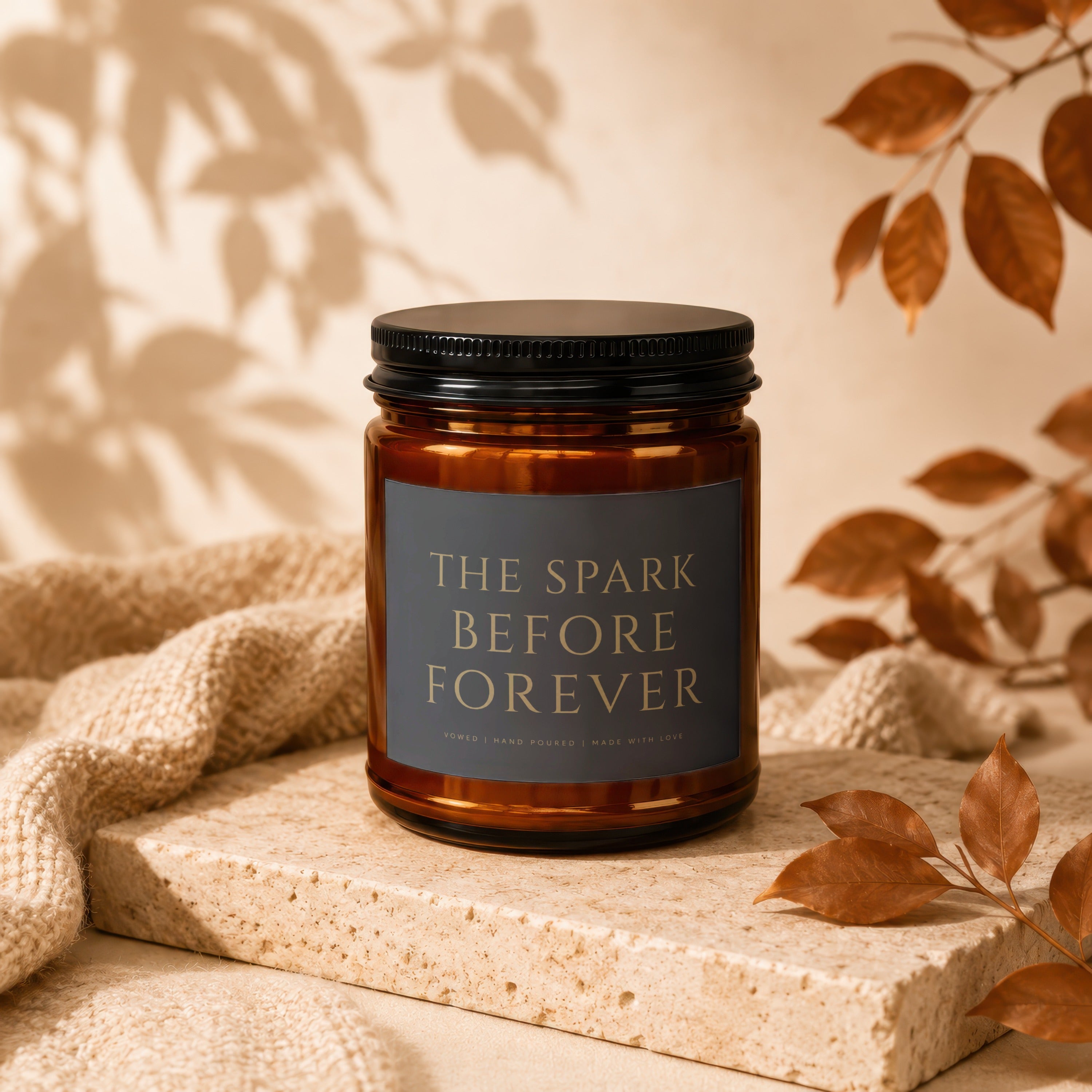 Amber candle with black lid, label reads "The Spark Before Forever".