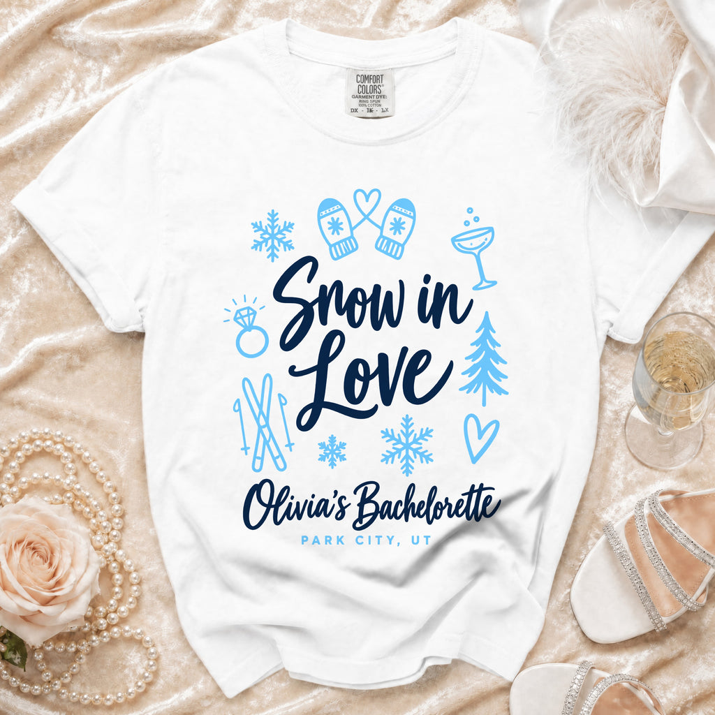 A white t-shirt features blue text reading Snow in Love, Olivia's Bachelorette, Park City, UT, surrounded by winter and bachelorette graphics.