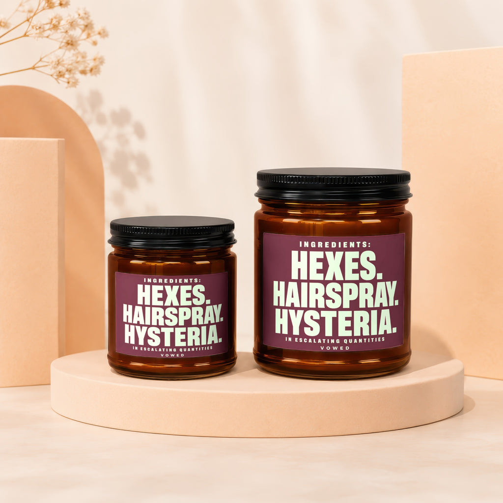 Two amber jars with purple labels reading "HEXES. HAIRSPRAY HYSTERIA. IN ESCALATING QUANTITIES VOWED".