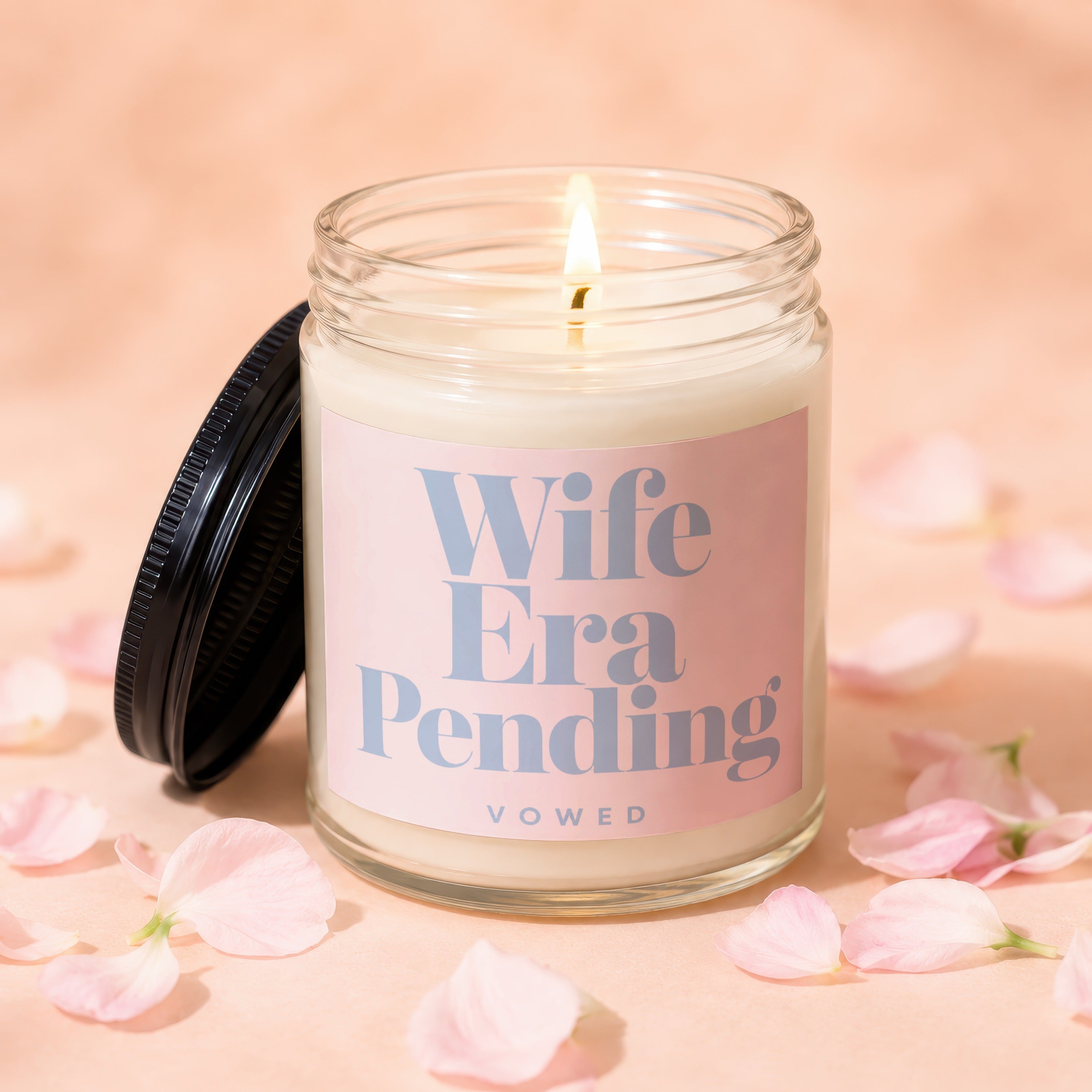 Lit candle in glass jar with pink label reading "Wife Era Pending VOWED."