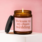 Amber jar candle with lit wick and black lid, reads "Welcome to my chaos wedding".