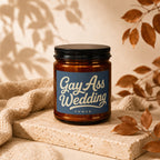 Amber jar candle with blue label reading "Gay Ass Wedding Vowed".