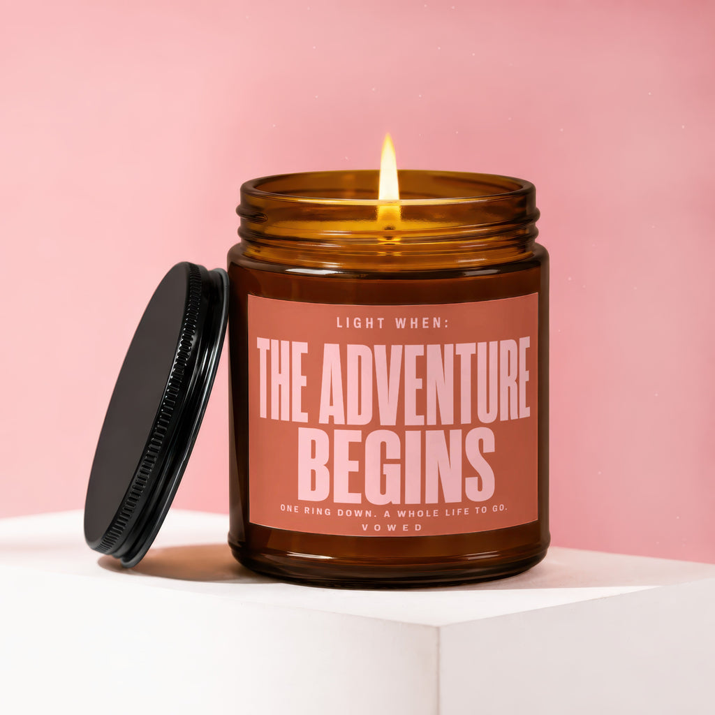 Amber glass candle with lit flame and text "THE ADVENTURE BEGINS".