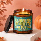 Amber candle with teal label reading "STATUS: BURNING BRIGHT FOR OUR FUTURE".
