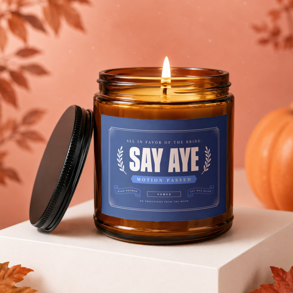 Amber candle with "Say Aye Motion Passed" label, lid off.