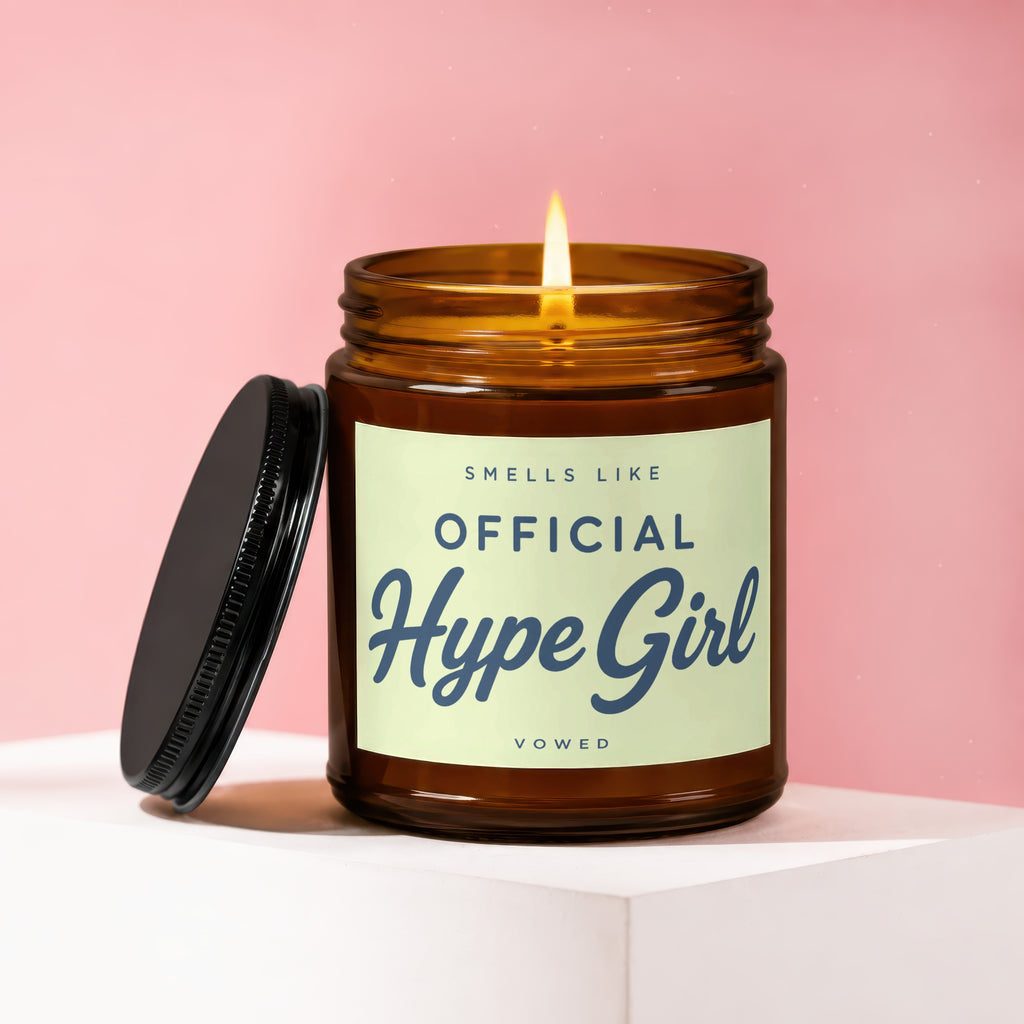 Candle with lit wick, black lid, and label that says "Smells Like Official Hype Girl Vowed".