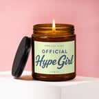 Candle with lit wick, black lid, and label that says "Smells Like Official Hype Girl Vowed".