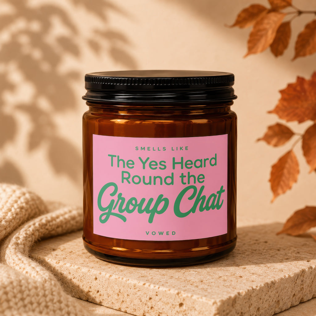 Brown glass candle with pink label reading "The Yes Heard Round the Group Chat"