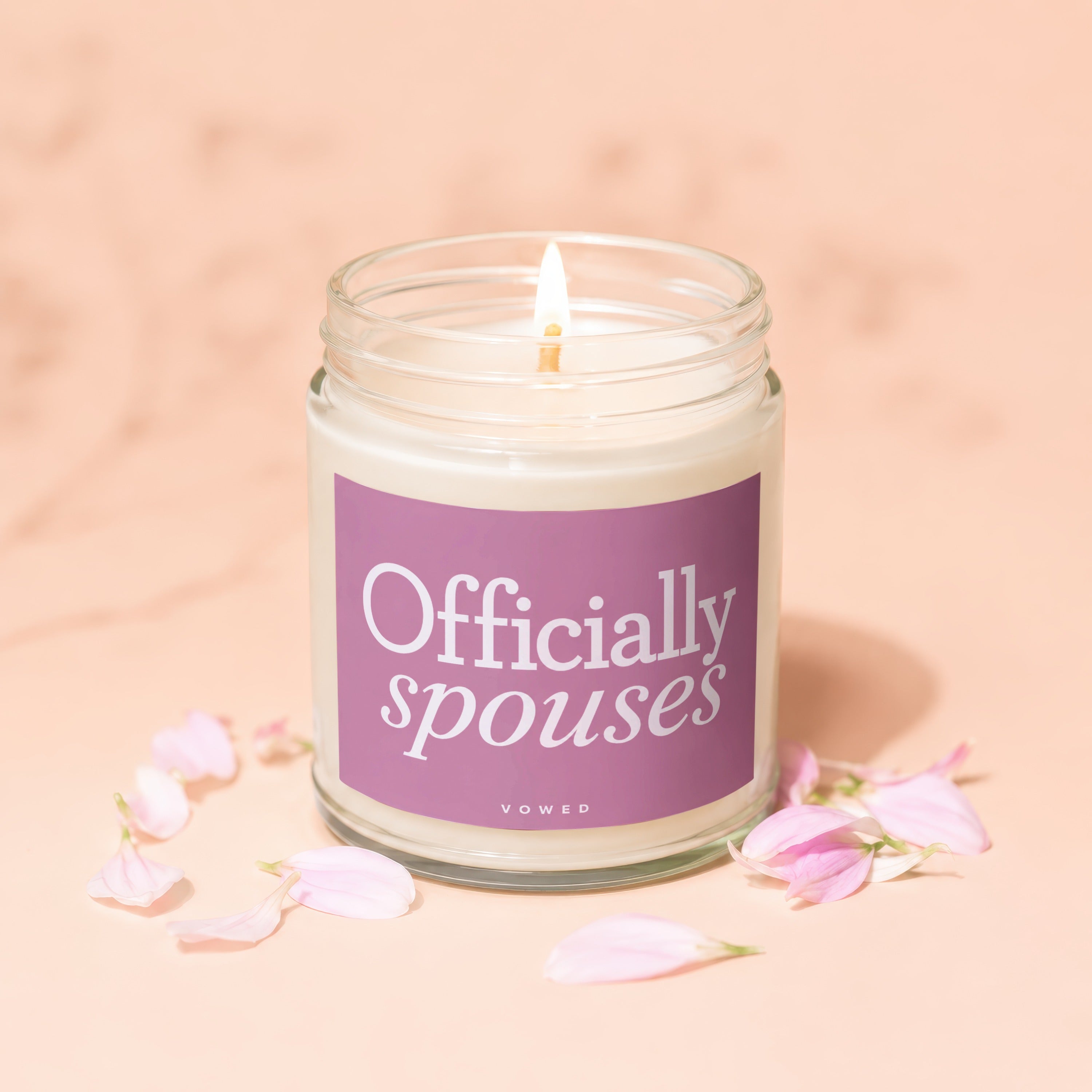 Glass jar candle with "Officially spouses" text on a purple label, surrounded by petals.