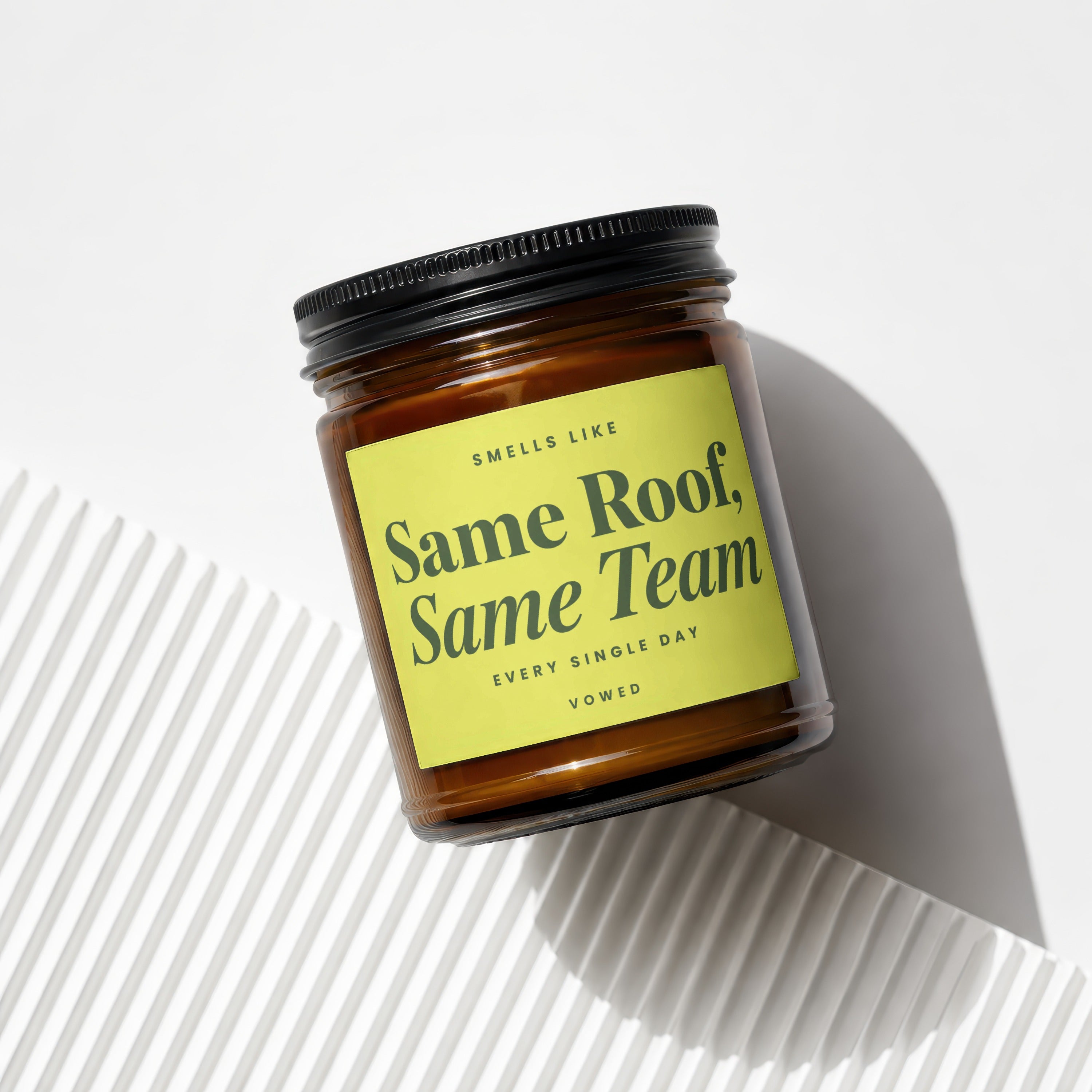 Amber jar candle with black lid labeled "Smells Like Same Roof, Same Team".