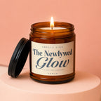 Amber candle with lid off, lit flame, and label "The Newlywed Glow".