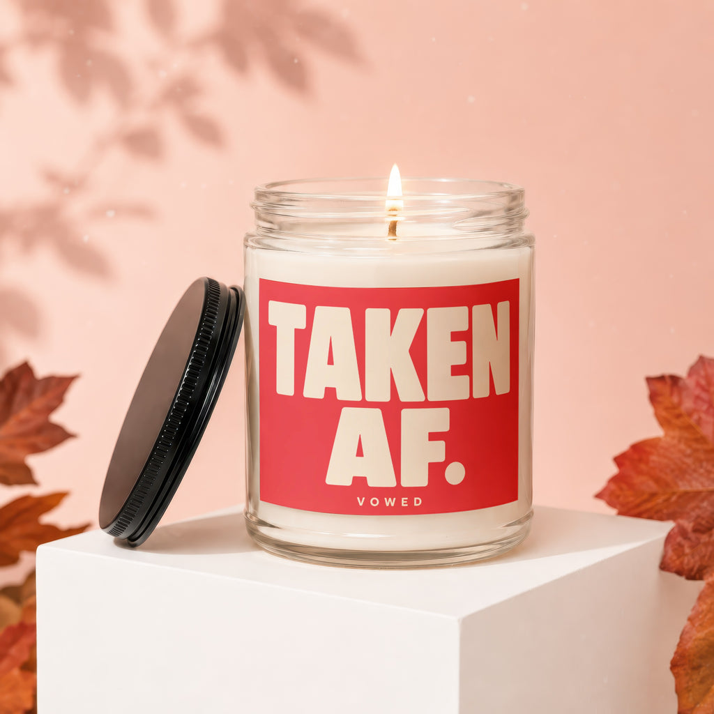 Lit candle in glass jar. Red label reads "TAKEN AF. VOWED".