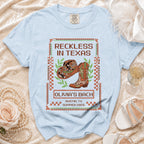 Light blue t-shirt with "Reckless in Texas Olivia's Bach Austin, TX Summer 2026" design.