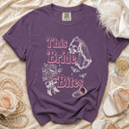 Purple t-shirt with "This Bride Bites" text, skull bride graphic, bouquet, and ring.
