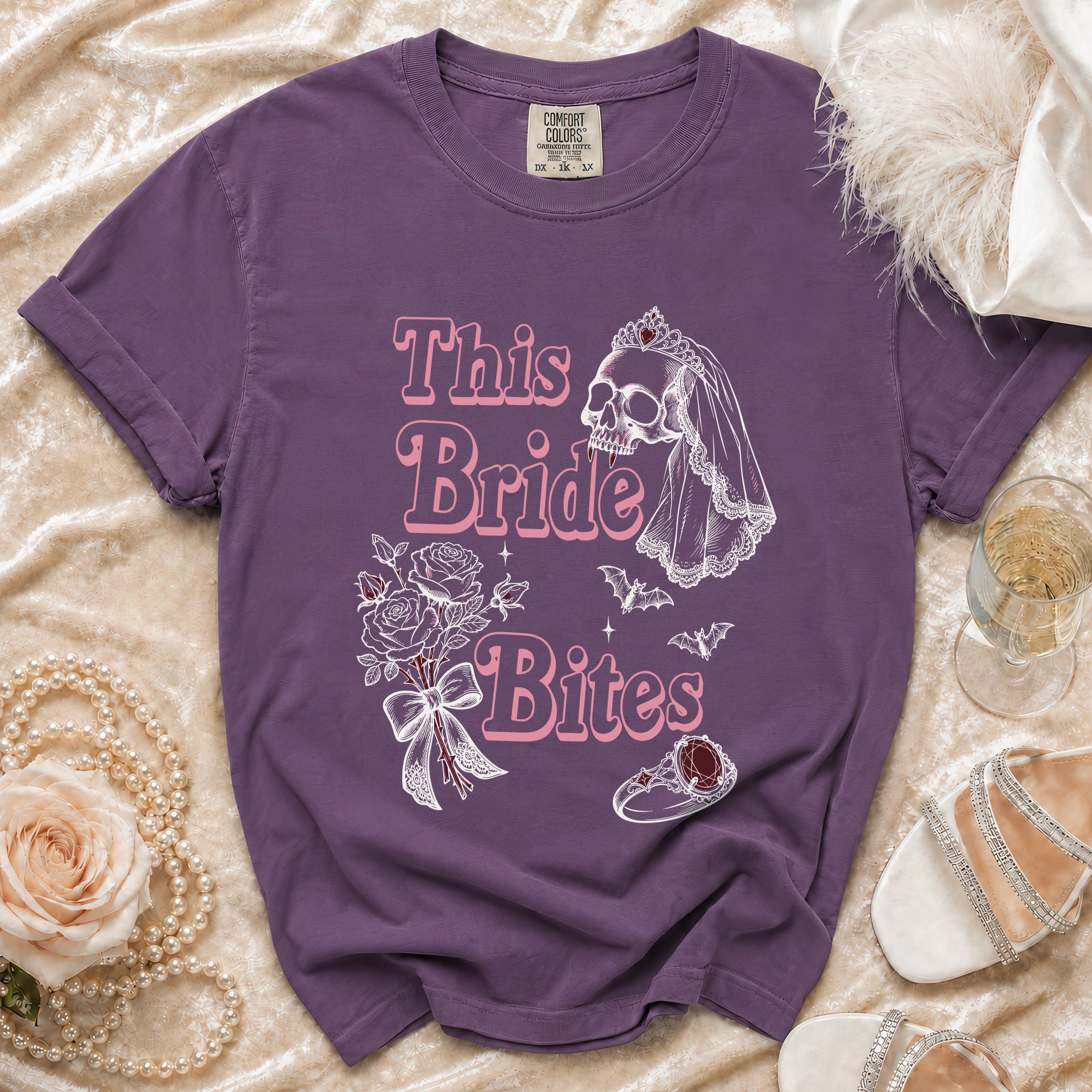 Purple t-shirt with "This Bride Bites" text, skull bride graphic, bouquet, and ring.