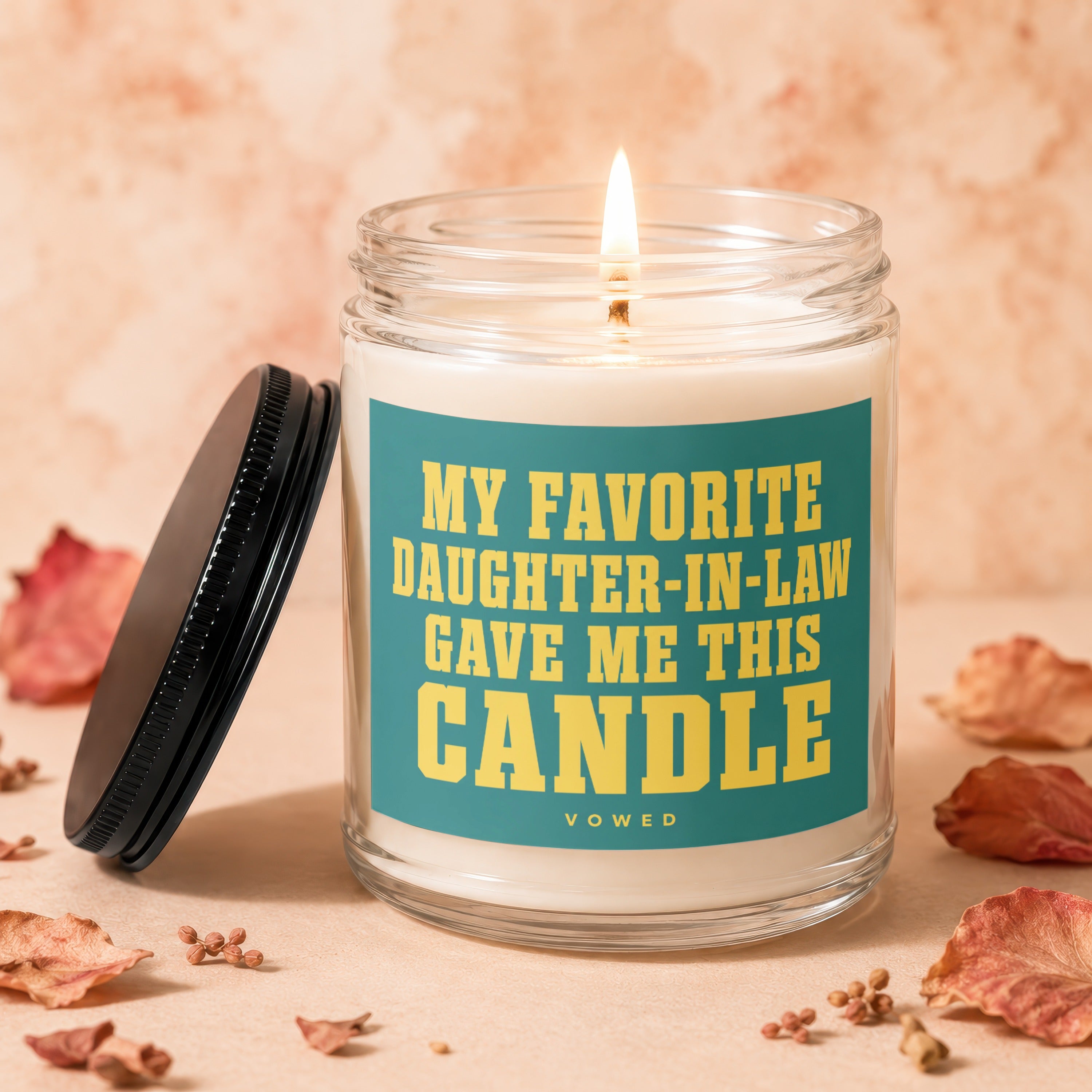 Glass candle with lit wick, black lid, and text "MY FAVORITE DAUGHTER-IN-LAW GAVE ME THIS CANDLE".