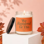 Glass candle with lit wick and lid to the side, features text "We Registered for This."