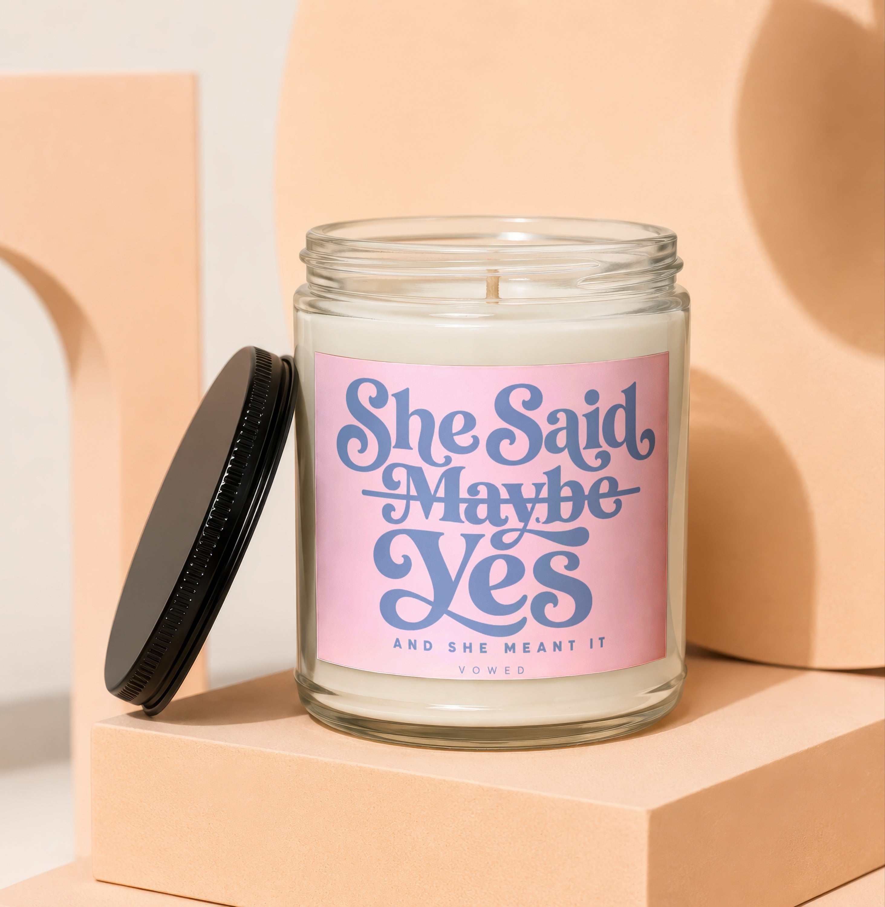 Candle with pink label reading "She Said Maybe Yes And She Meant It Vowed."