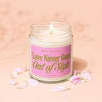Glass jar candle with lit wick featuring pink label that reads "Smells Like Love Never Goes Out of Style."
