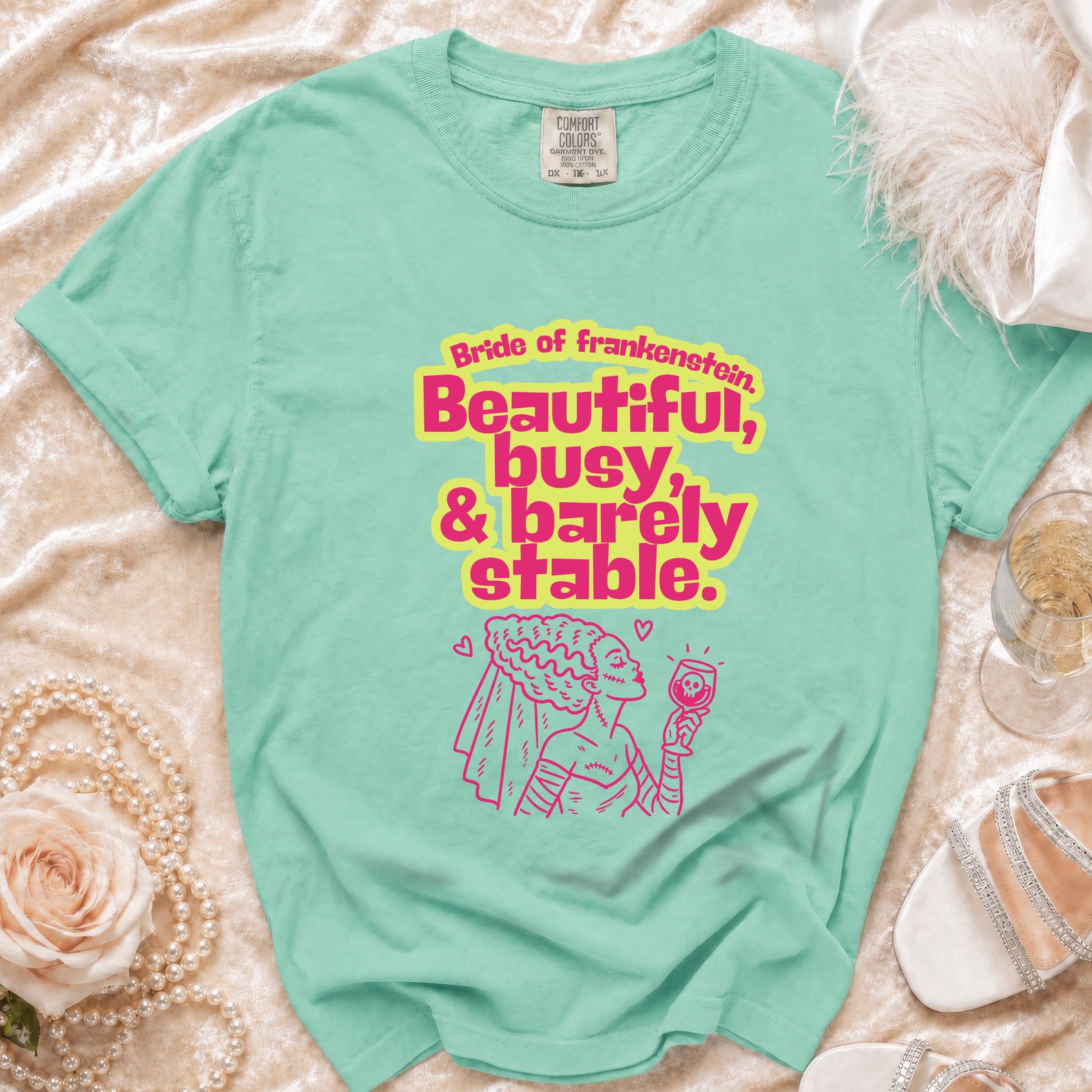 Teal t-shirt with pink "Bride of Frankenstein, Beautiful, busy, & barely stable" text and illustration.
