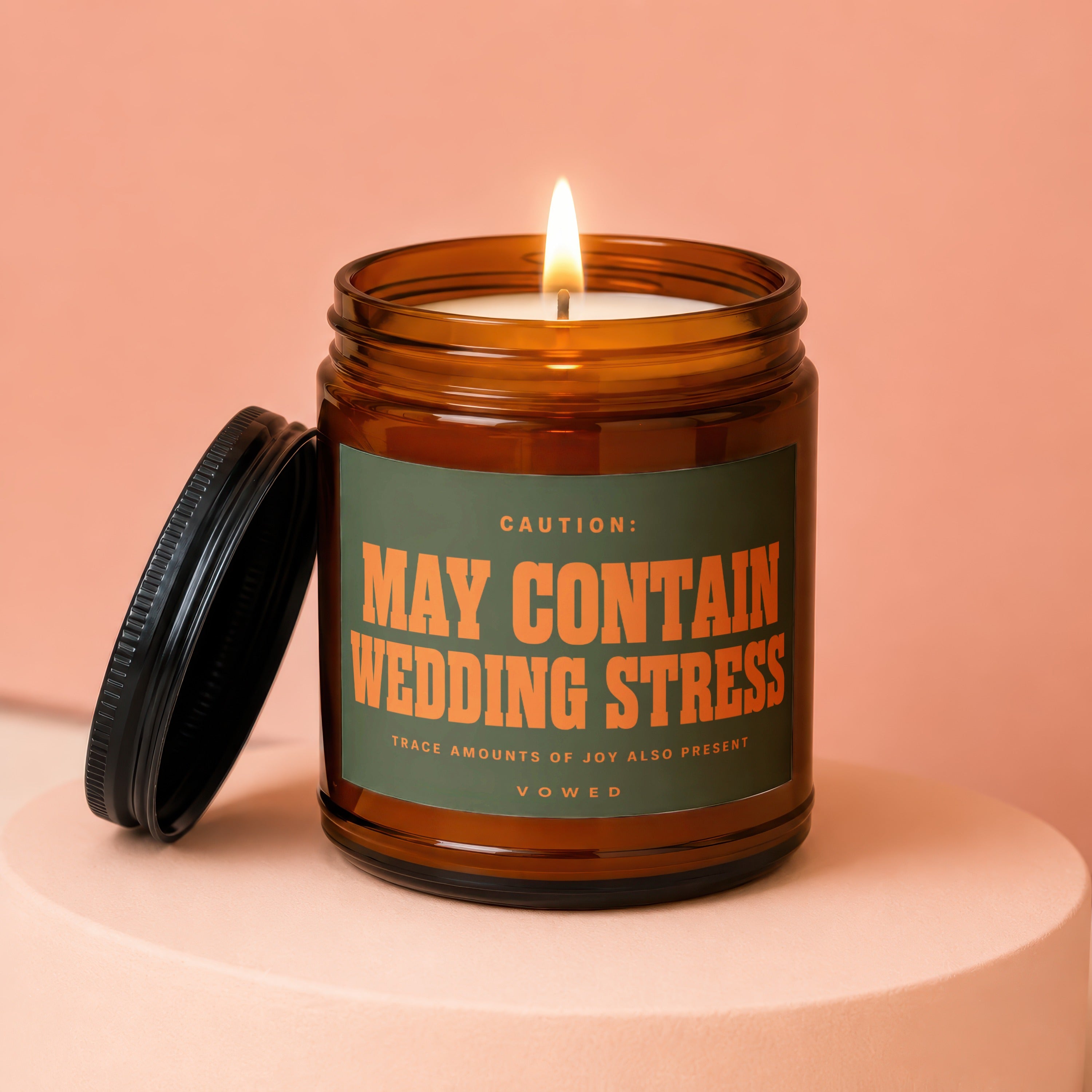 Amber jar candle with green label reading "CAUTION: MAY CONTAIN WEDDING STRESS".